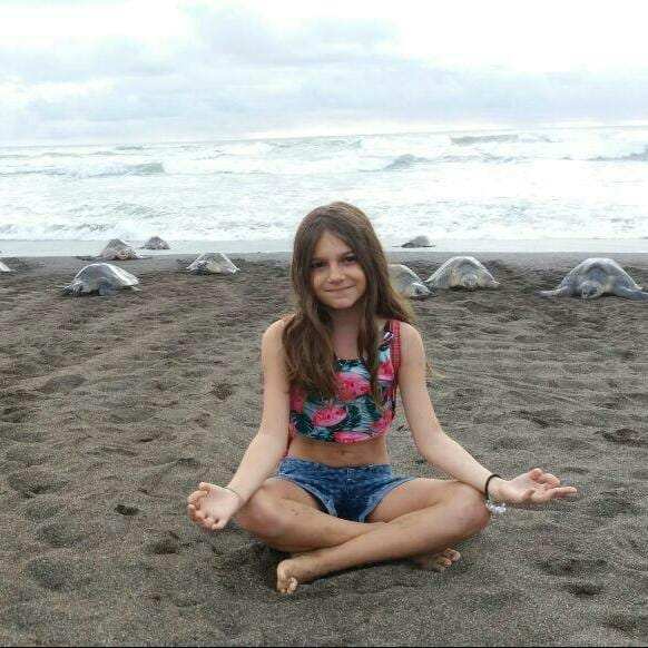 Girl sitting cross-legged on the beach with sea turtles behind her